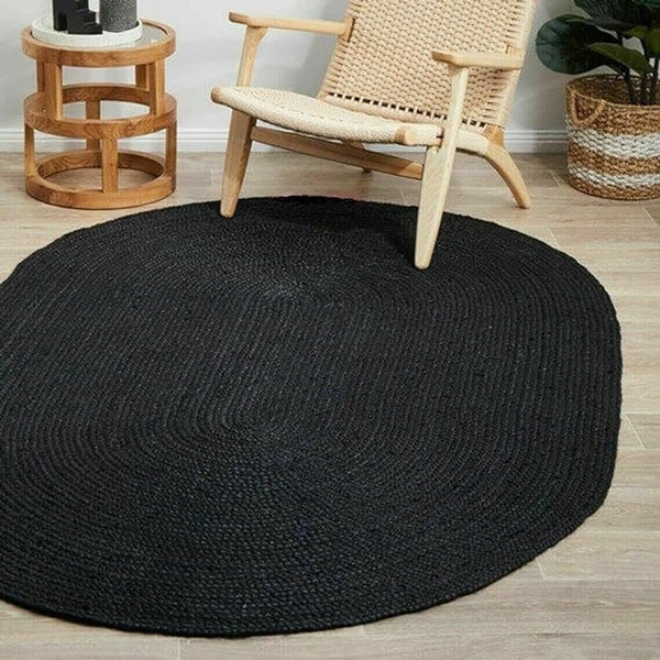Black round rug on a wooden floor with a wicker chair and small table in the background.