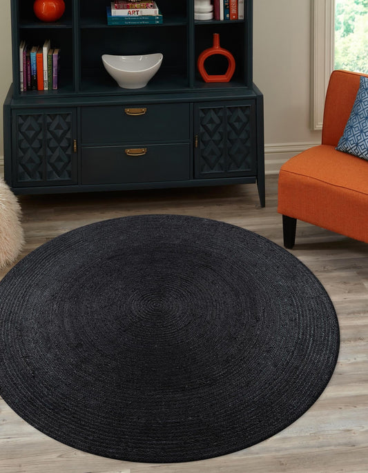 Round black rug in a living room with an orange chair and dark blue cabinet.
