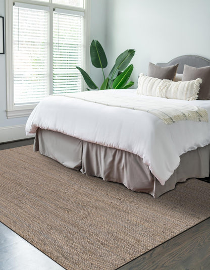 Neatly made bed with white bedding and gray headboard in a room with a large window and plant.