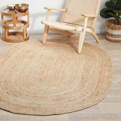 oval jute rug on a wooden floor with a woven chair and side table in the background.