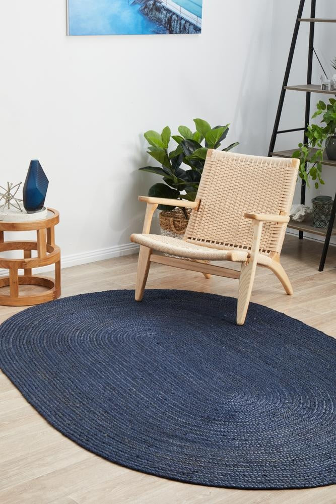 Oval blue rug on a wooden floor with a wicker chair and plants in the background.