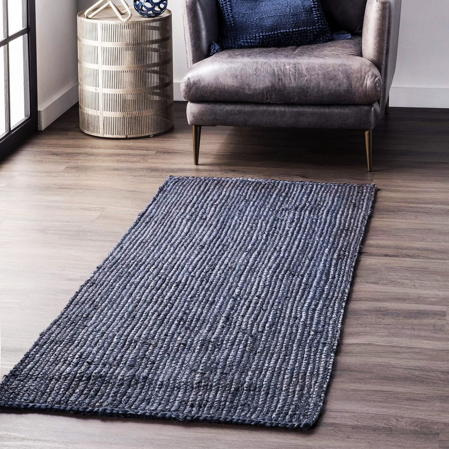 Gray textured rug on a wooden floor with a chair and side table in the background.
