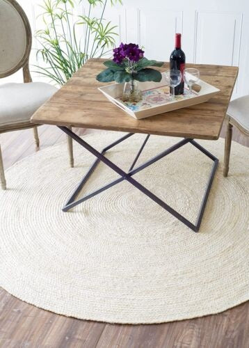 Wooden coffee table with metal legs on a round beige rug, surrounded by chairs.