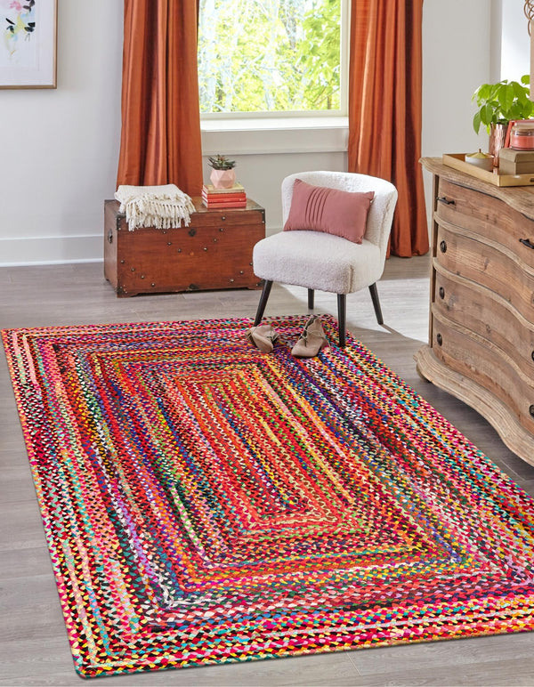 Multicolored braided rug in a room with a chair, chest, and curtains.