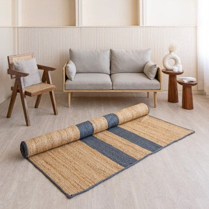 Rolled jute rug with striped pattern on a light wooden floor in a modern living room setting.