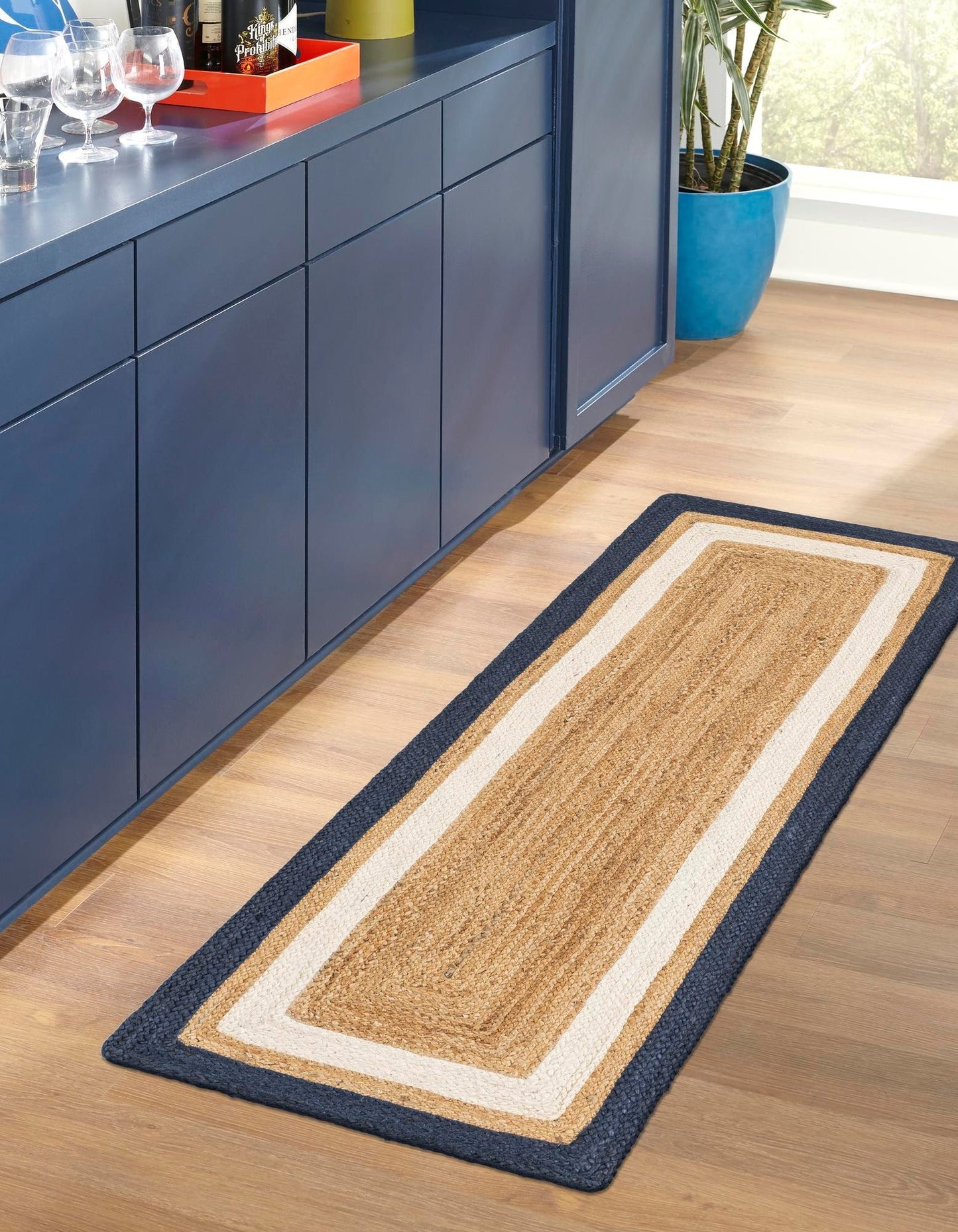 Long rectangular jute rug with a blue border on a wooden floor next to blue cabinets.
