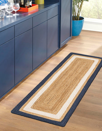 Long rectangular jute rug with a blue border on a wooden floor next to blue cabinets.