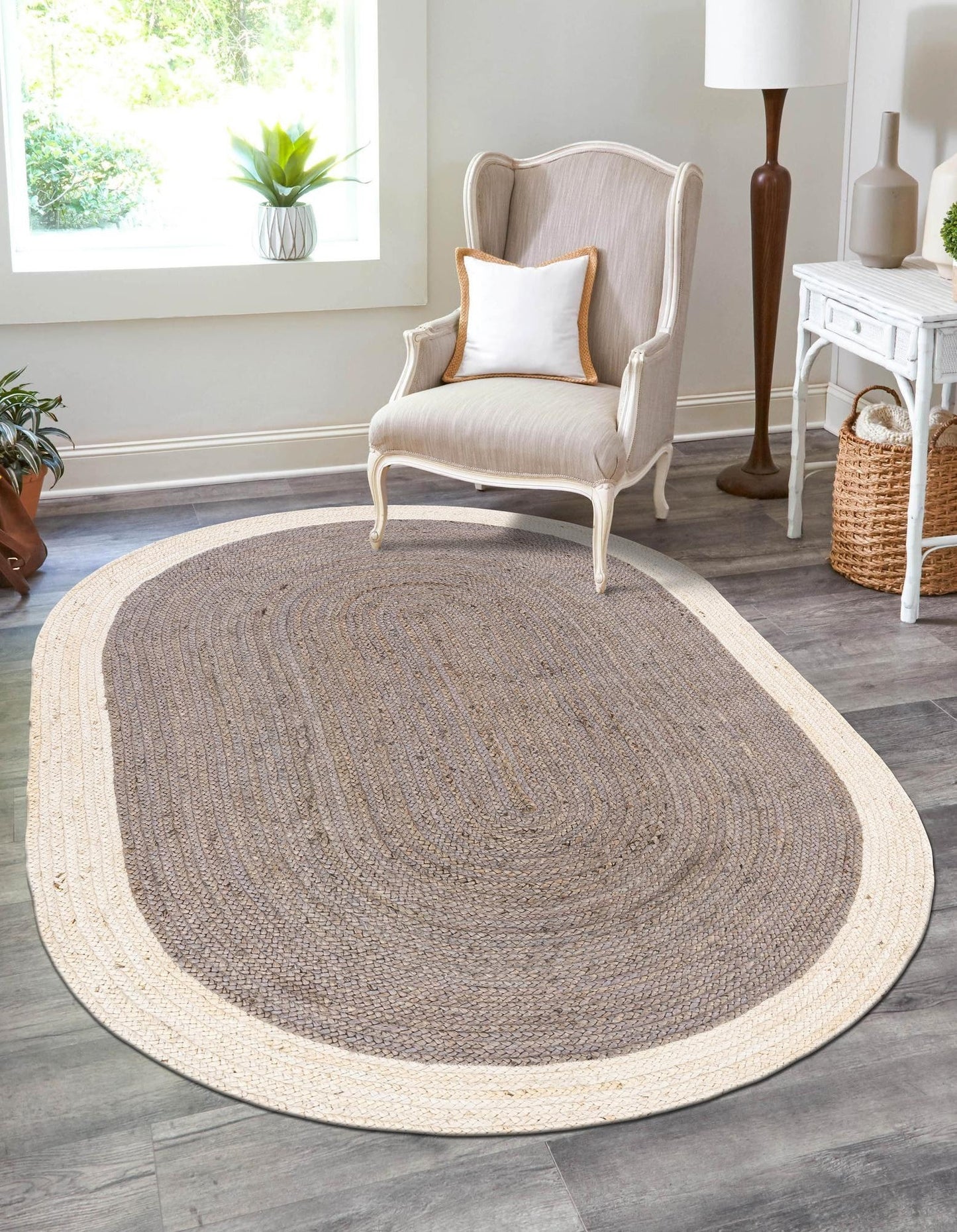 Oval-shaped braided rug on a wooden floor with a chair and decor items in the background.
