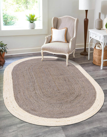 Oval-shaped braided rug on a wooden floor with a chair and decor items in the background.