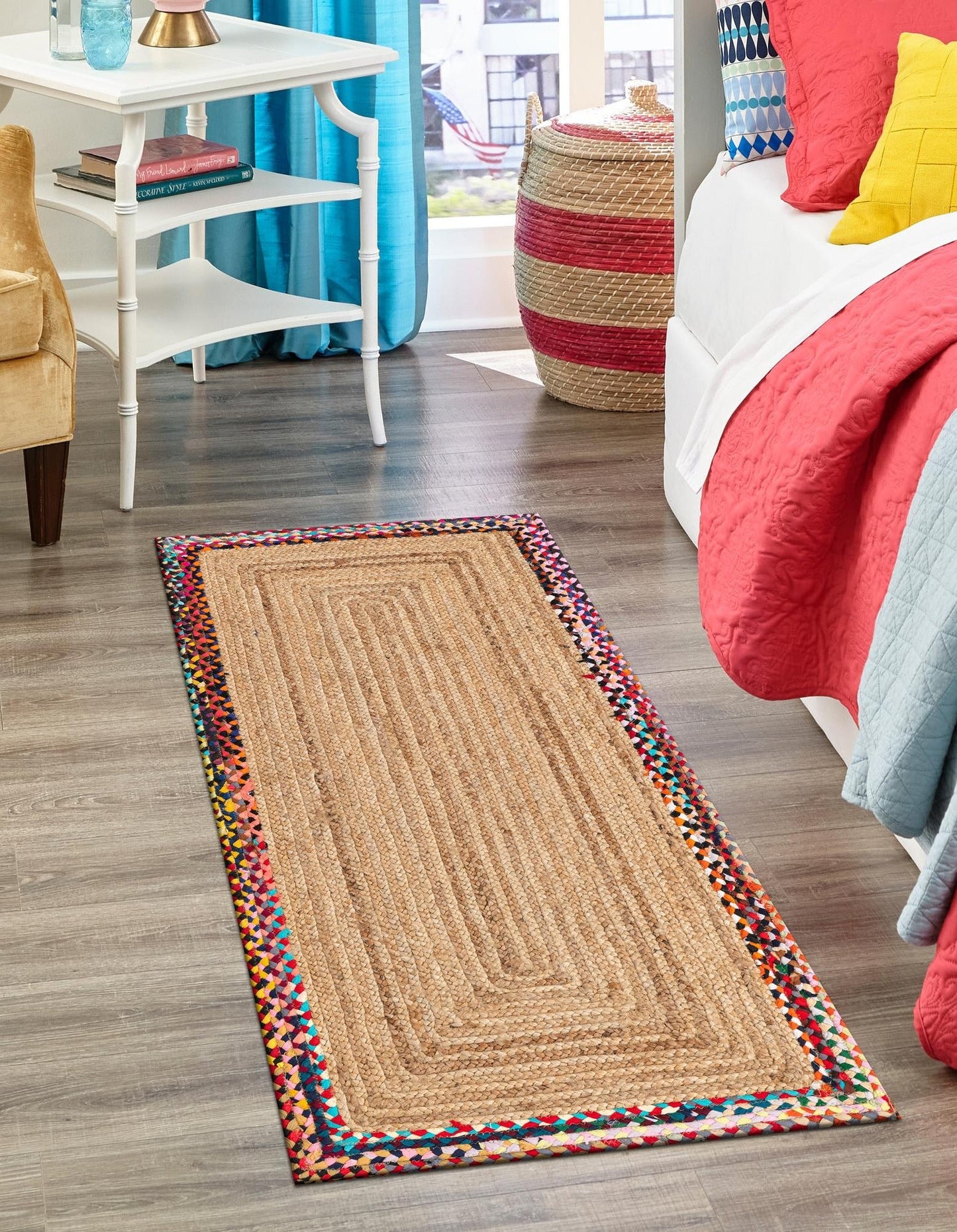 Colorful braided rug on a wooden floor with a bed and furniture in the background.