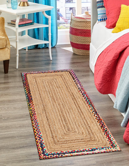 Colorful braided rug on a wooden floor with a bed and furniture in the background.