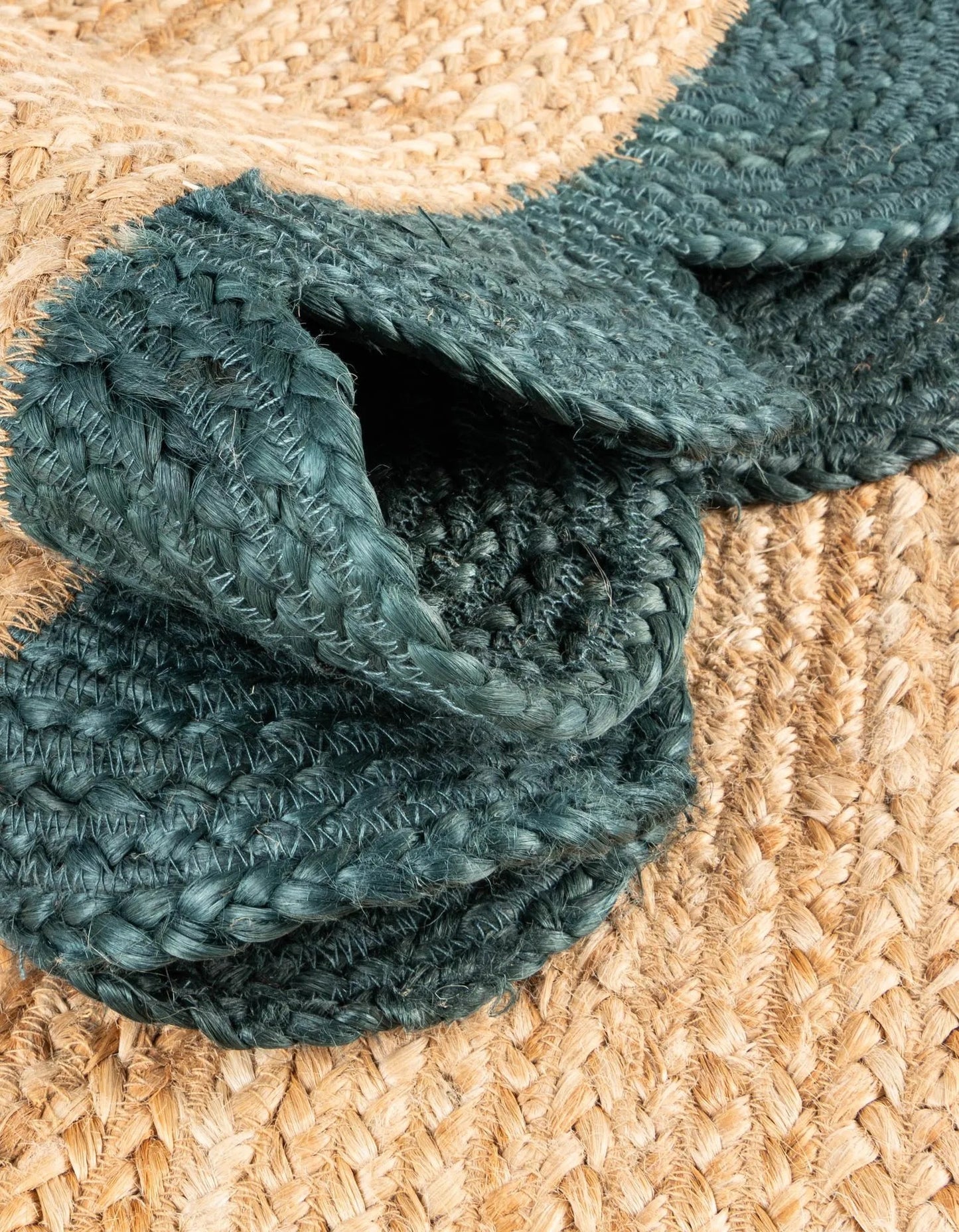 Close-up of natural jute rug with dark green scalloped border, showing thick braided texture and durable handcrafted weave