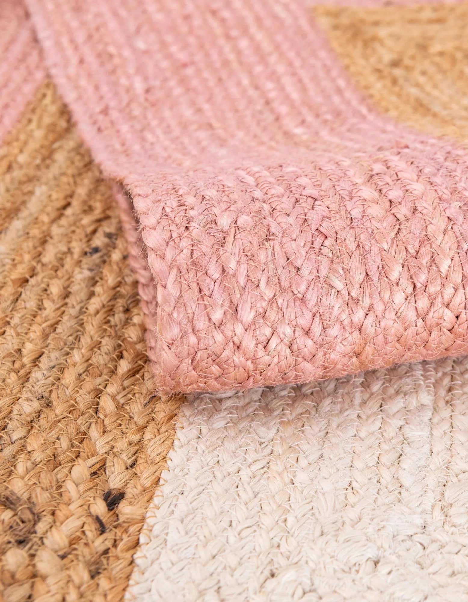 Close-up of pink braided rug with beige and white rugs underneath