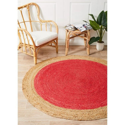 Round red and natural jute rug on a wooden floor with a rattan chair and plant in the background.