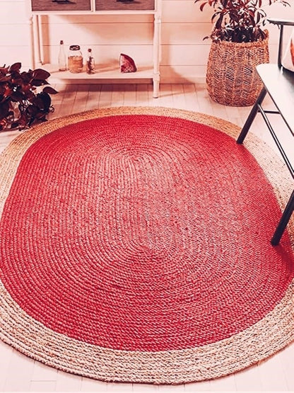Round red braided rug on a wooden floor with plants and a shelf in the background.
