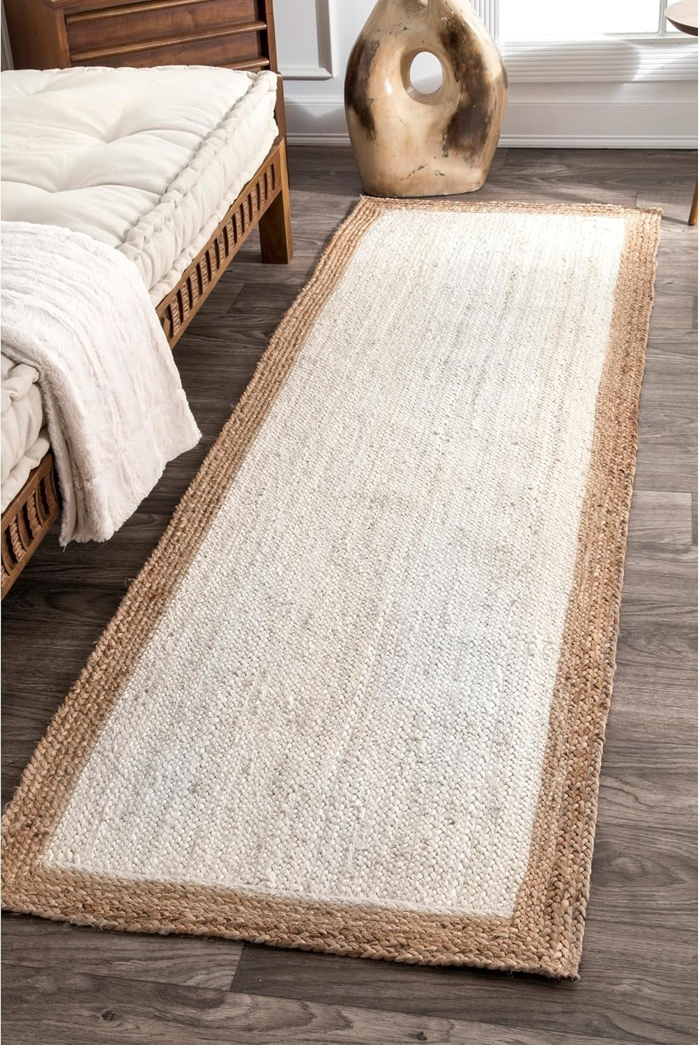 Long rectangular rug with a natural border on a wooden floor, next to a wooden bench.