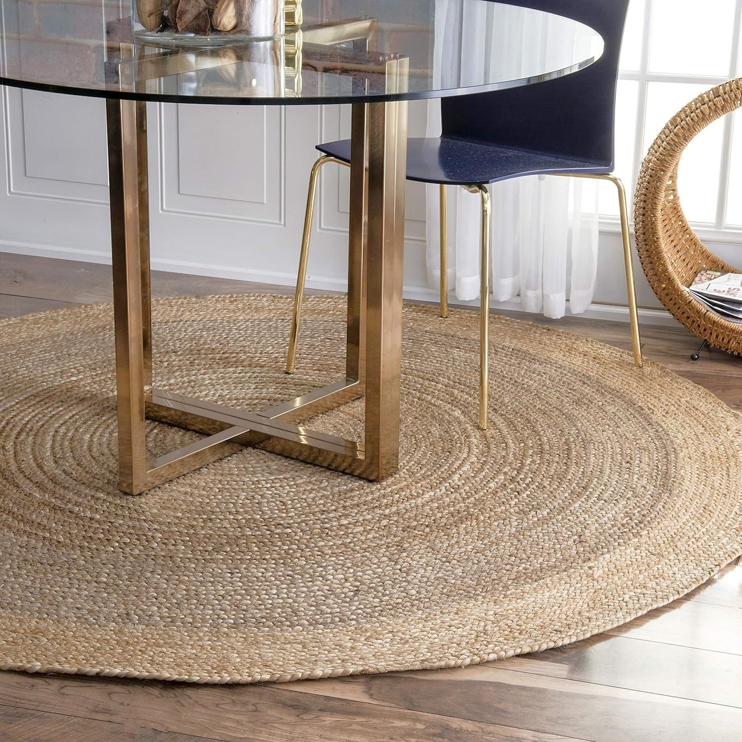 Dining room with a glass table on a round jute rug, surrounded by chairs.