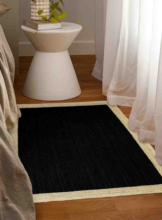 Black rug on a wooden floor with a white side table and plant in the background.