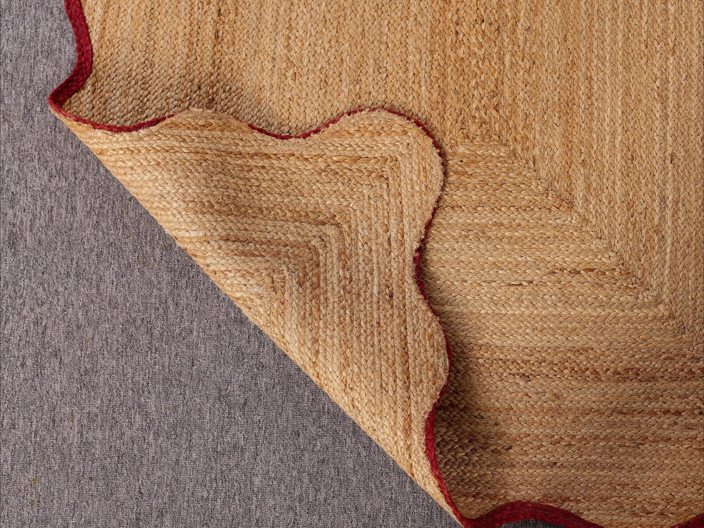 Close-up of a textured beige and red rug corner on a gray surface