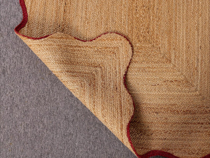 Close-up of a textured beige and red rug corner on a gray surface