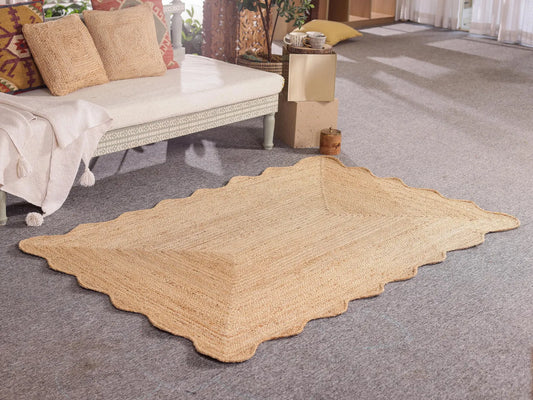 Beige woven rug on a gray carpeted floor with a wicker chair and cushions in the background.