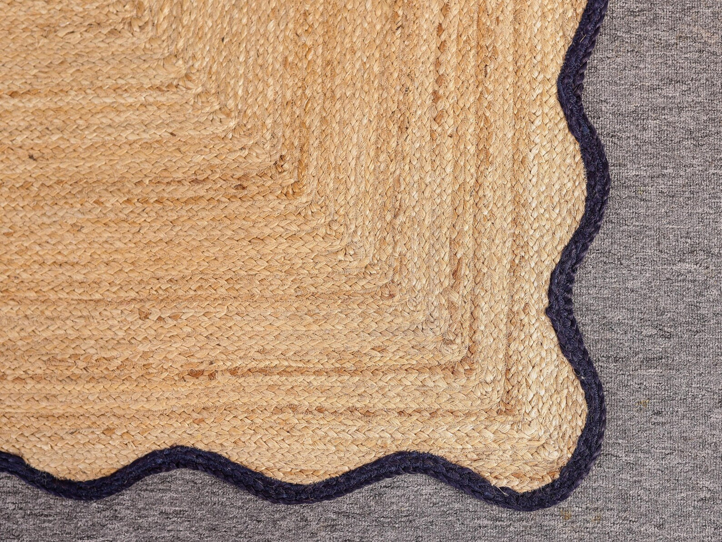 Close-up of a textured beige rug with a dark border on a gray surface