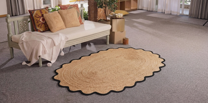 Beige woven rug on a gray carpeted floor with a couch and pillows in the background.