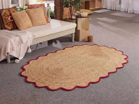 Oval woven rug with red border on a gray carpeted floor